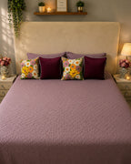Dusty mauve quilted bedsheet set styled with floral and burgundy decorative cushions